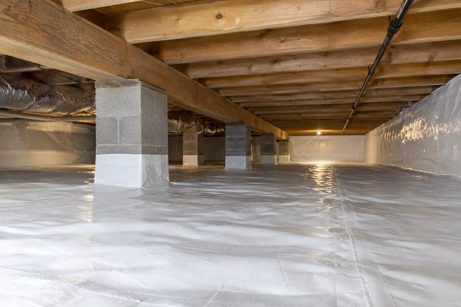 Crawl space with a white vapor barrier over the floor and walls